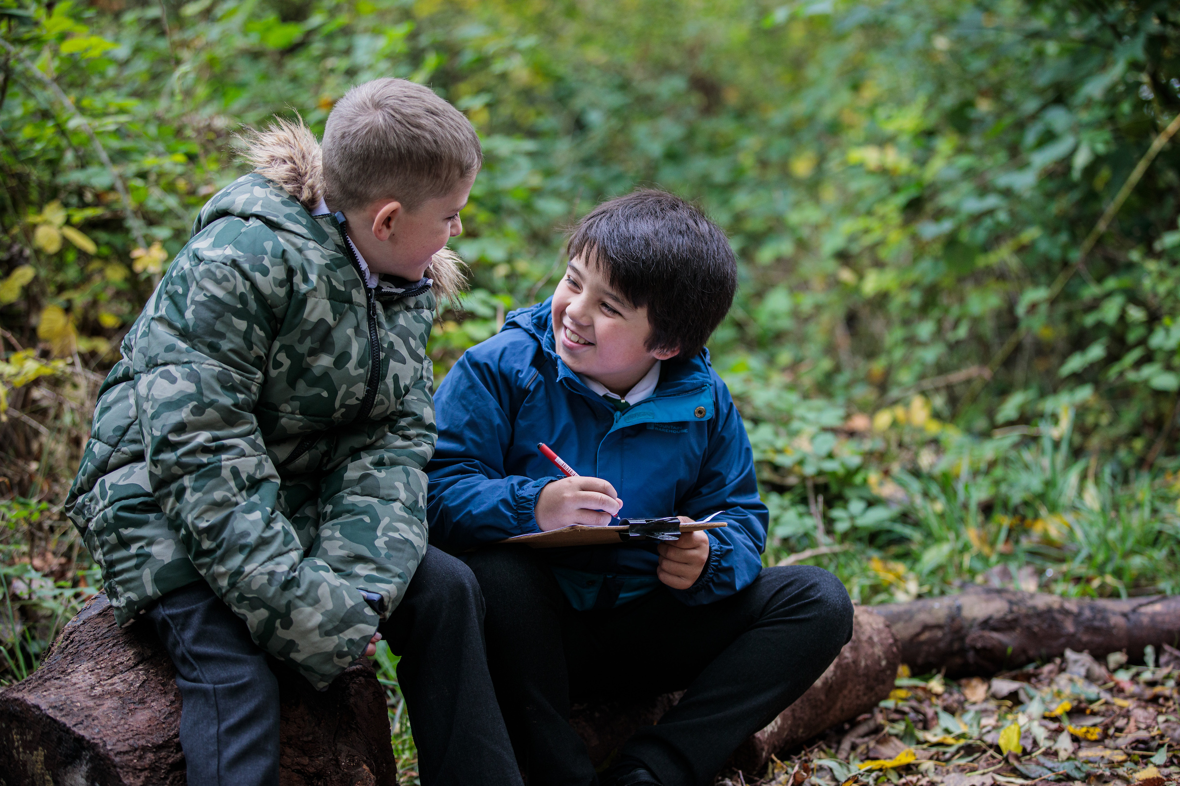 two primary age boys working together in outdoor woodland setting