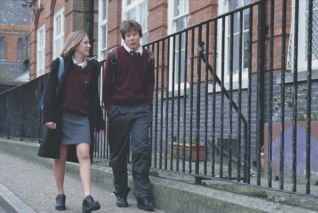 Secondary age male and female students in school uniform walking outside of school.