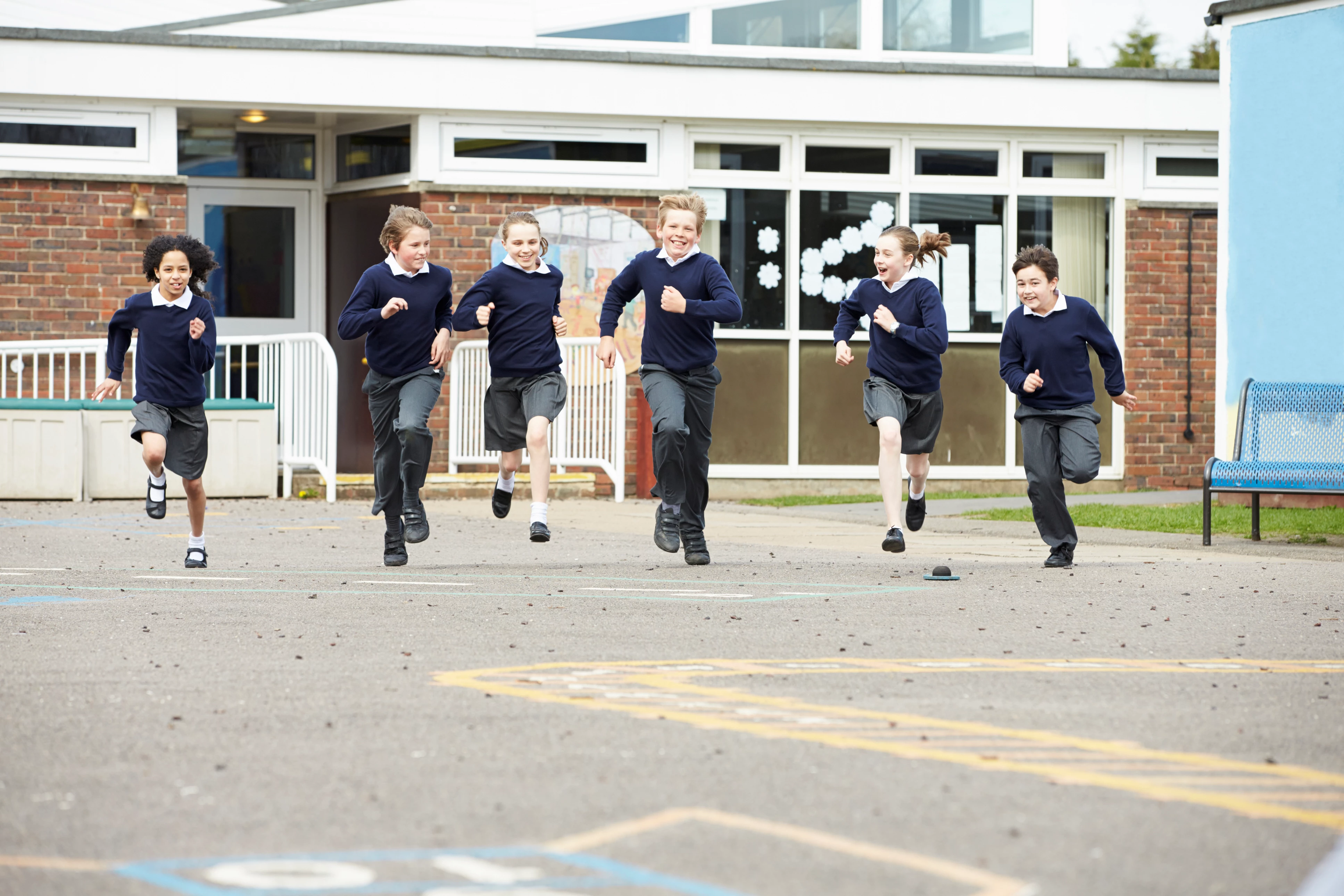 Group of 6 children running across a school playground