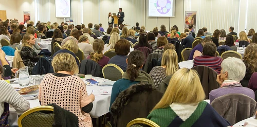Large group of conference delegates sitting listening to keynote speaker.
