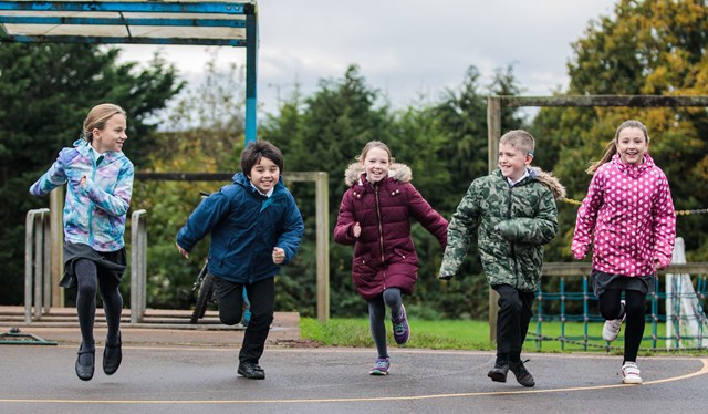 5 children running across the playground towards the camera - all wearing their winter coats