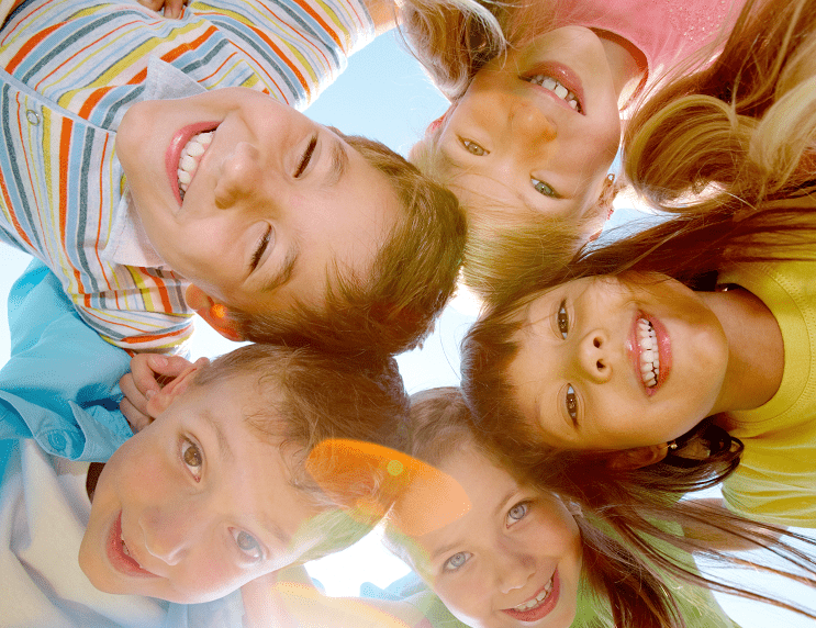 5 young children all smiling and looking down towards the camera in a circle