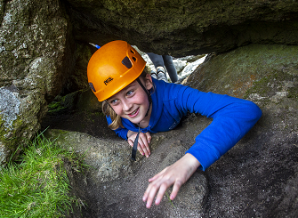 Smiling girl wearing an orange hard hat whilst climbing through and over rocks on Dartmoor.